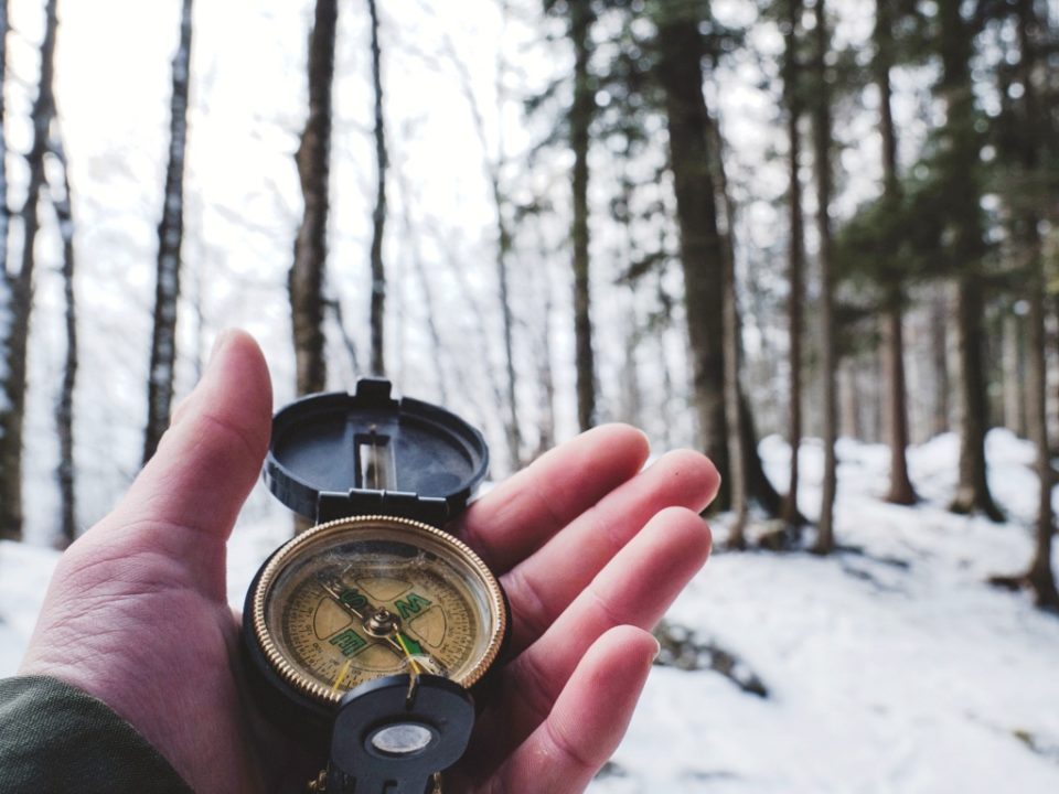 Nordic leadership – a man holding a compass in a snowy pine forest, leading the way